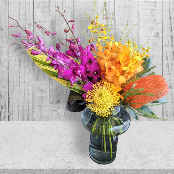 Colorful tropical bouquet in a glass vase with purple, orange, and yellow blooms