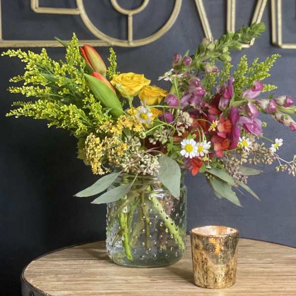 Mixed bouquet in a glass jar with a small gold candle holder beside it