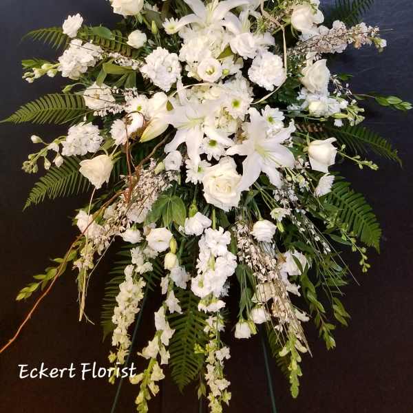 Tall white funeral spray with lilies, roses, and snapdragons