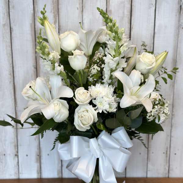 White lilies and roses arranged in a glass vase with a white ribbon