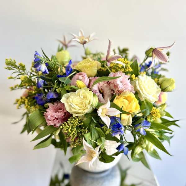 Mixed bouquet of pastel roses, blue flowers, and pink blooms in a vase