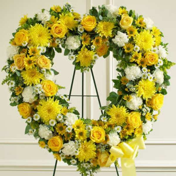 Heart-shaped floral wreath with yellow roses and white flowers on a stand