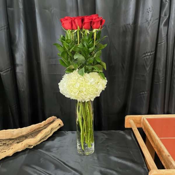Tall vase arrangement with red roses and a white hydrangea cluster