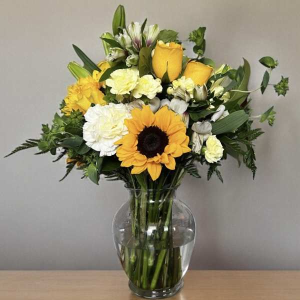 Bouquet of yellow roses, sunflowers, and white carnations in a glass vase