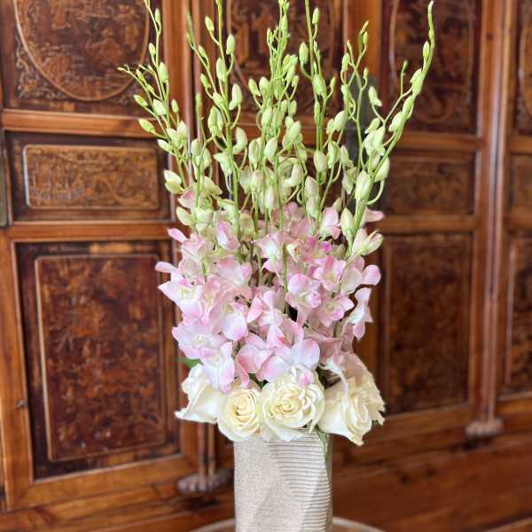 Tall floral arrangement with pink orchids and white roses in a textured vase
