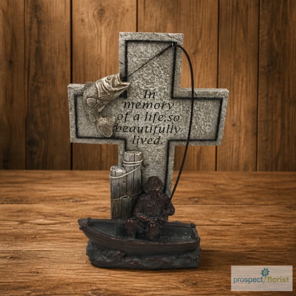 Memorial cross figurine with a fisherman and boat on a wooden surface
