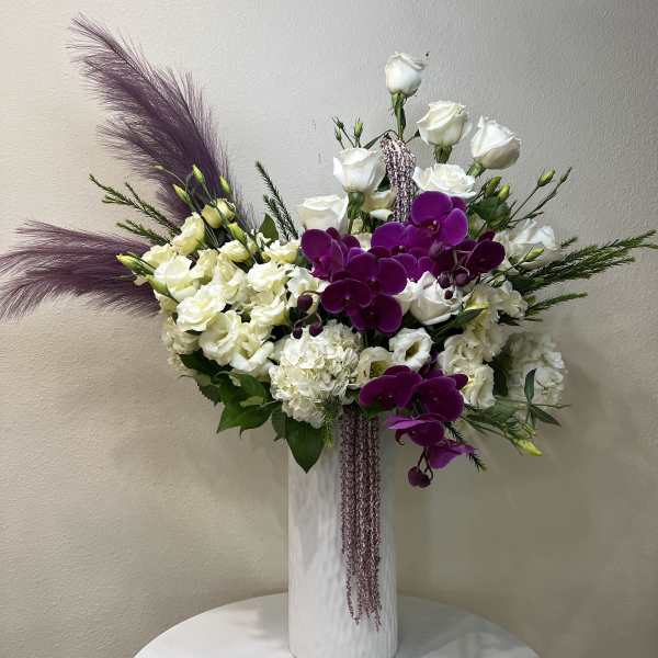 White roses and purple orchids in a tall white vase