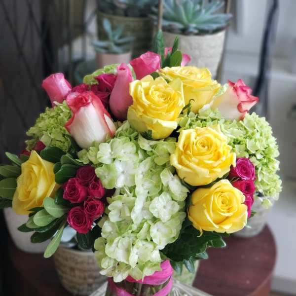 Bouquet of yellow and pink roses with pale green hydrangeas in a glass vase