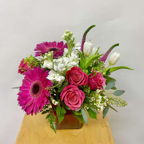 Pink gerberas and roses arranged in a low vase with white tulips.