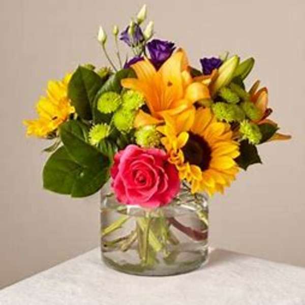 Mixed bouquet with sunflowers, lilies, roses, and purple blooms in a glass vase