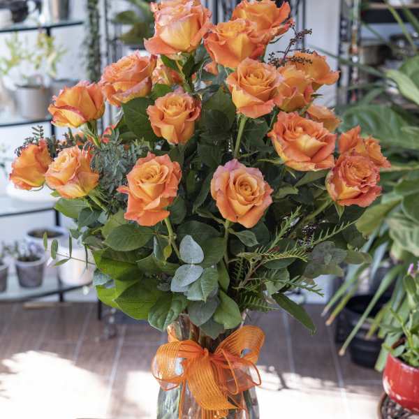 Orange roses in a clear glass vase with an orange ribbon