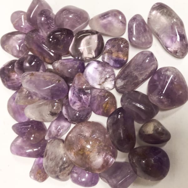 Pile of polished purple amethyst stones on a white surface