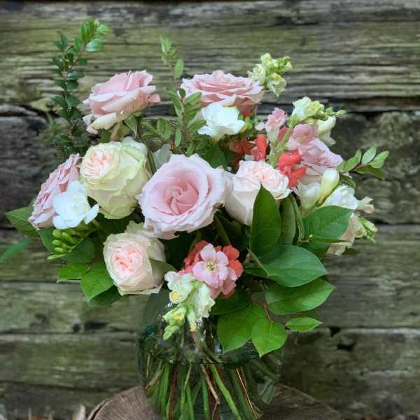 Pink and white roses in a glass vase with greenery