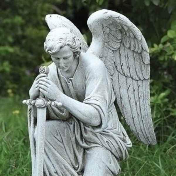Stone angel statue kneeling in grass with folded wings