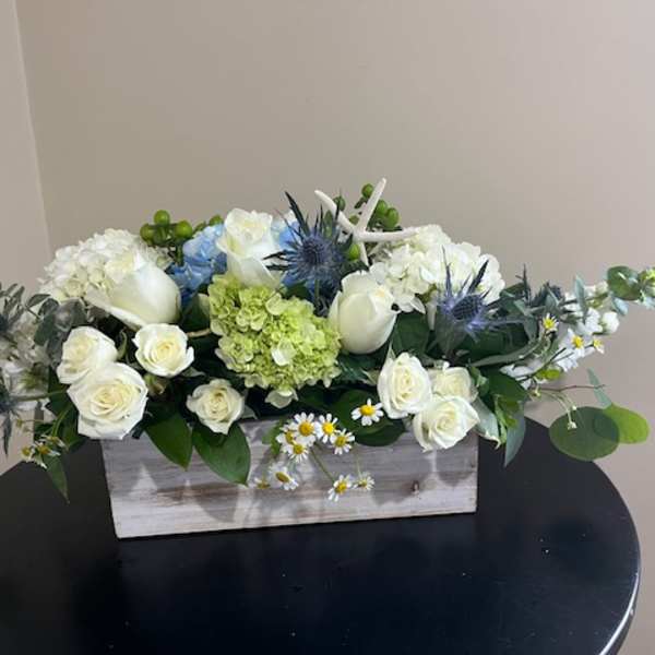 White roses and hydrangeas arranged in a wooden box with blue thistle accents.