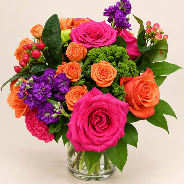 Bright mixed bouquet of pink, orange, and purple flowers in a clear glass vase