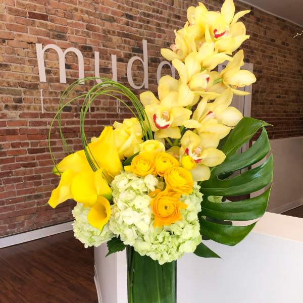 Yellow orchids, calla lilies, and roses arranged in a tall glass vase