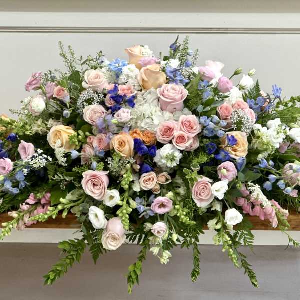 Large pastel floral casket spray with roses and blue blooms