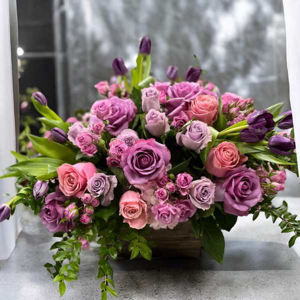 Pink and lavender roses with purple tulips in a low rectangular container
