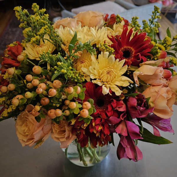 Mixed bouquet of yellow, red, and peach flowers in a glass vase