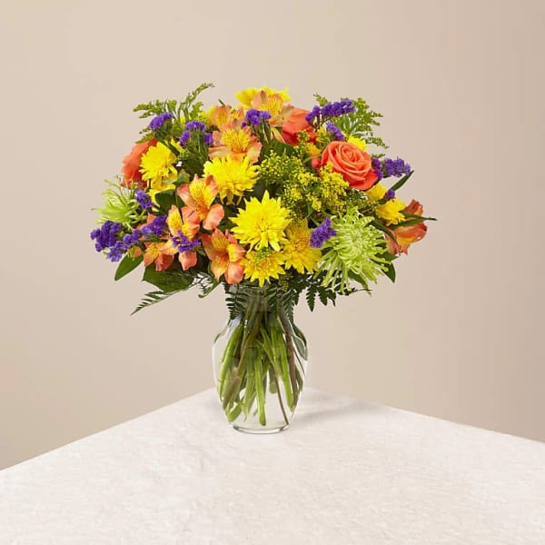 Mixed bouquet of yellow, orange, and purple flowers in a clear glass vase