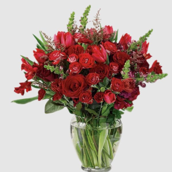 Red roses and tulips arranged in a clear glass vase