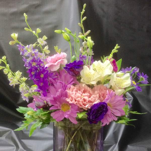 Mixed bouquet of pink, purple, and white flowers in a purple glass vase