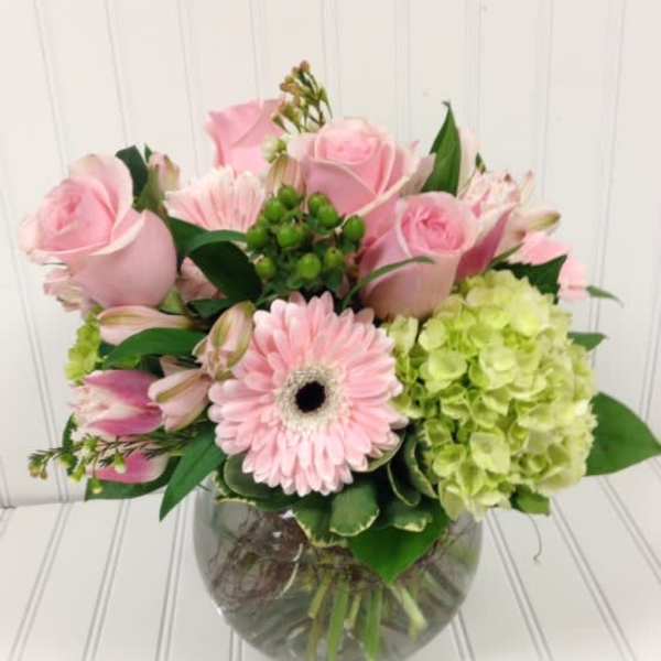Pink roses and a gerbera daisy in a glass vase with green hydrangea