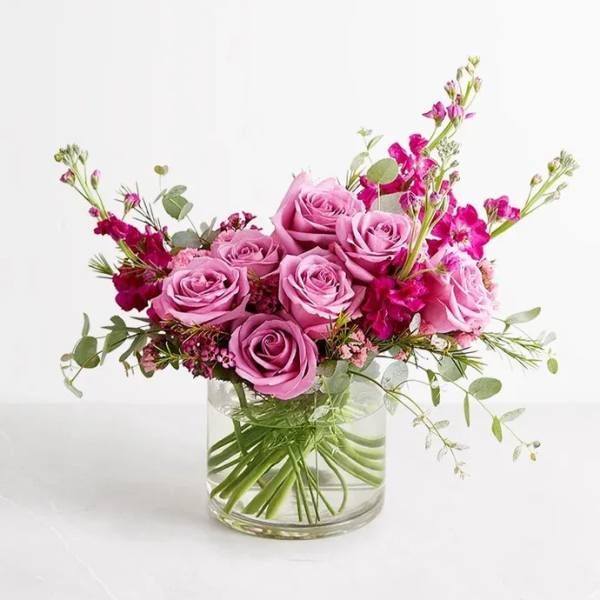 Pink roses and magenta flowers arranged in a clear glass vase