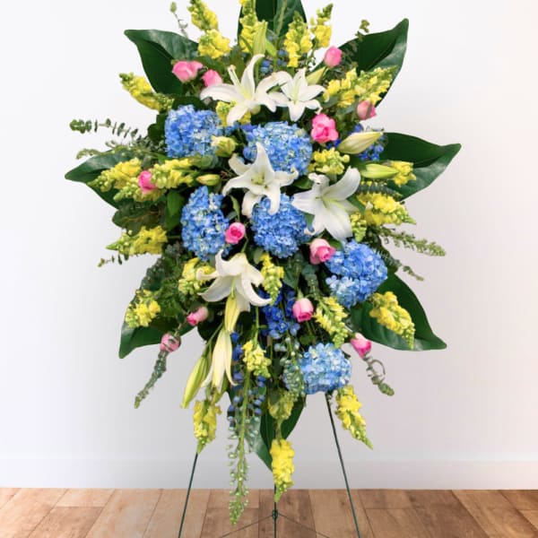 Standing floral spray with blue hydrangeas, white lilies, and yellow snapdragons