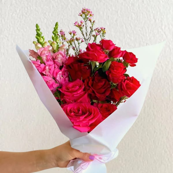 Handheld bouquet of red and pink roses wrapped in white paper