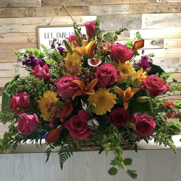 Mixed bouquet of pink roses, orange lilies, and yellow daisies in a basket