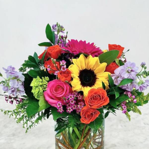 Colorful mixed bouquet in a clear glass vase with a sunflower and roses