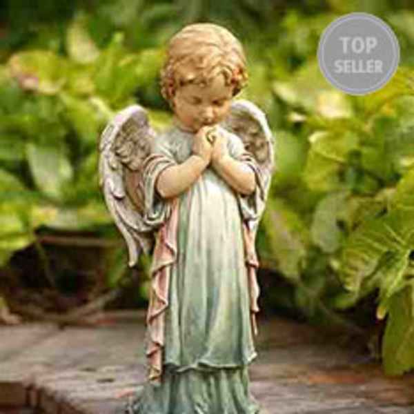 Small praying angel figurine in a garden setting