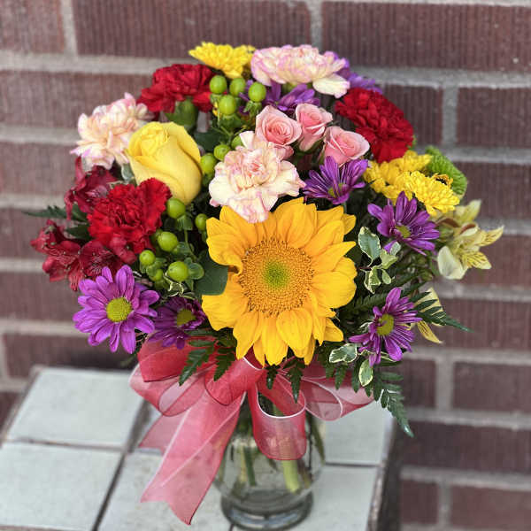 Mixed bouquet with sunflowers, roses, carnations, and daisies in a glass vase