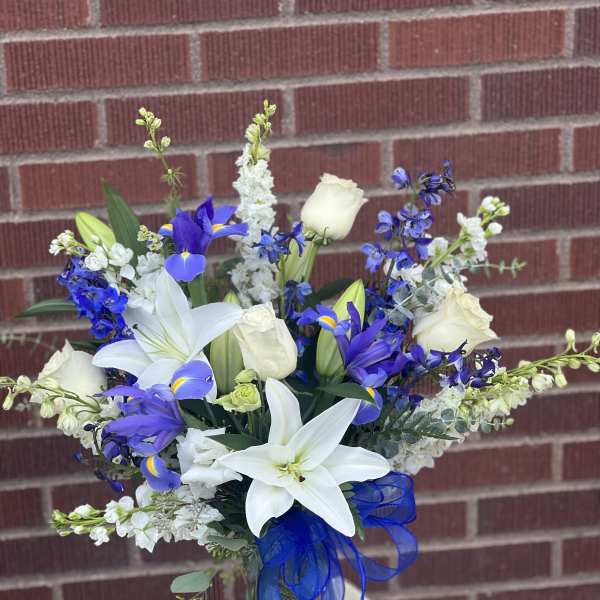 White lilies and blue-purple flowers in a glass vase with a blue ribbon