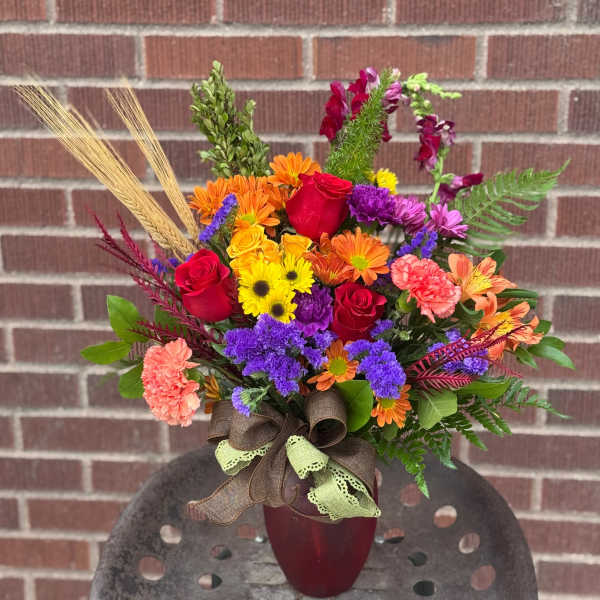 Colorful mixed bouquet in a burgundy vase with a ribbon bow
