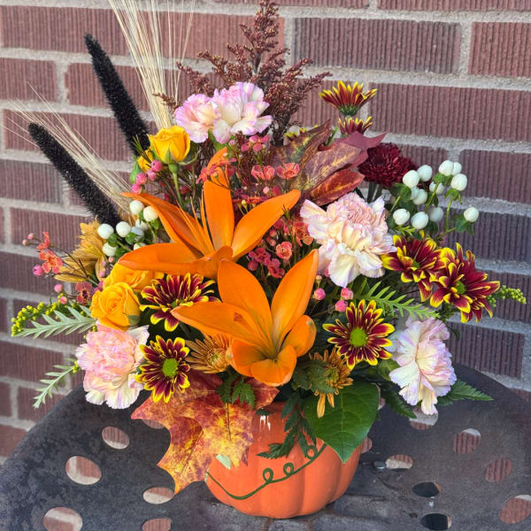 Autumn flower arrangement in an orange pumpkin container with lilies and mums