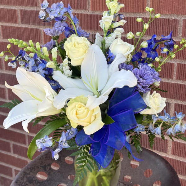 White lilies and pale roses in a glass vase with blue ribbon