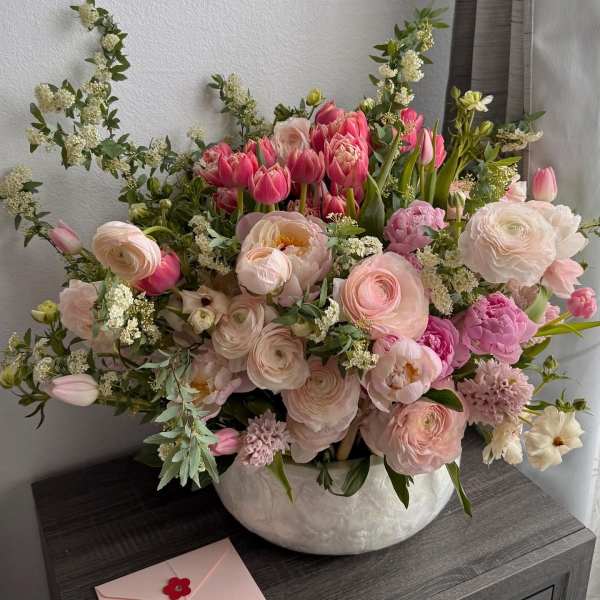 Pink and white mixed flower arrangement in a ceramic bowl with a card