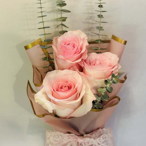 Bouquet of pink roses wrapped in blush paper with a lace ribbon