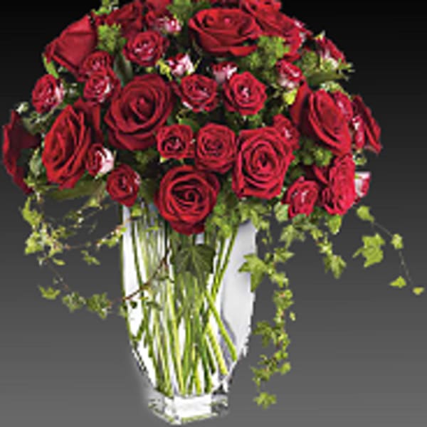 Red rose bouquet in a clear glass vase with trailing greenery