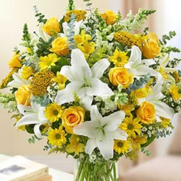 Arrangement of white lilies, yellow roses, and yellow daisies in a clear glass vase