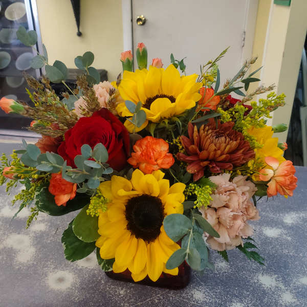 Mixed bouquet with sunflowers, roses, and carnations in a low vase