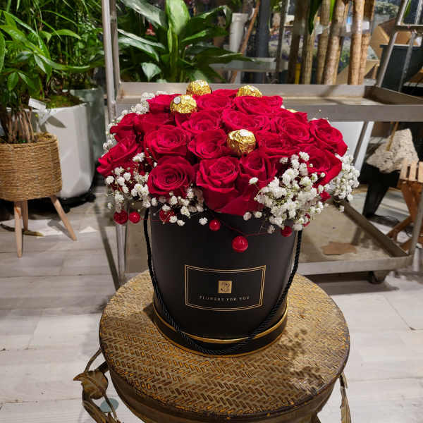 Red roses arranged in a black hatbox with gold-wrapped chocolates