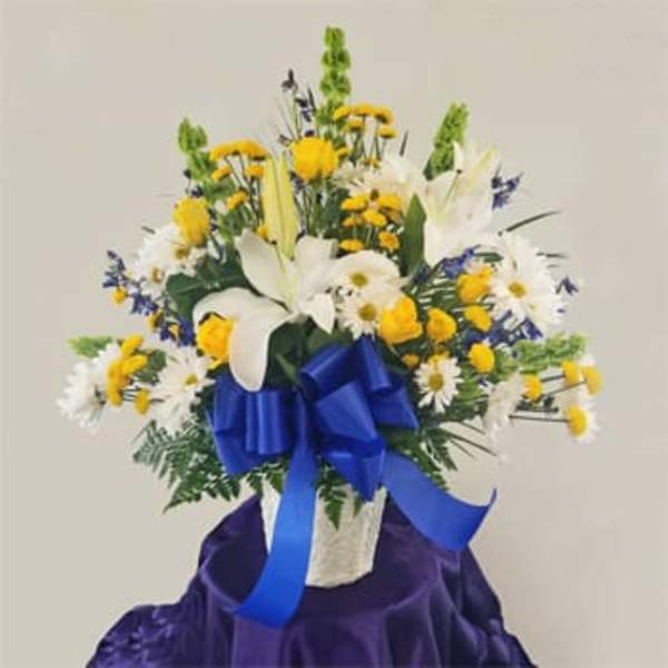 Bouquet of white lilies, yellow daisies, and blue flowers in a white basket