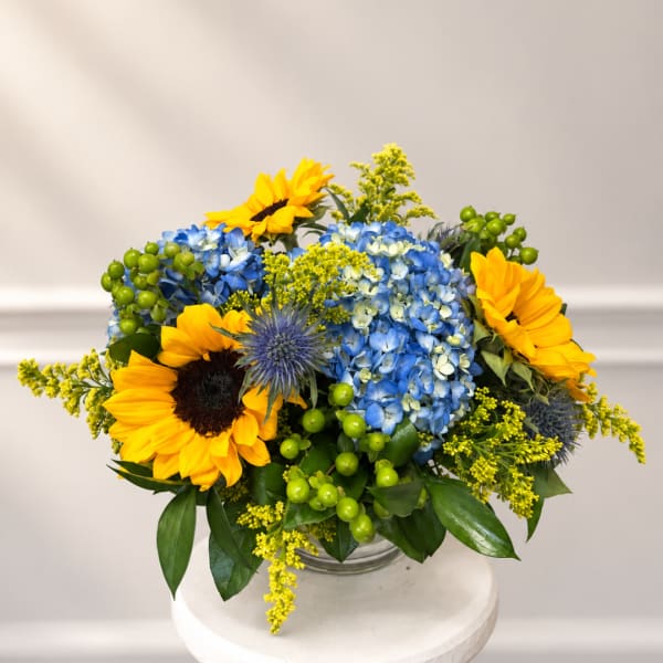 Sunflowers and blue hydrangeas arranged in a clear glass vase