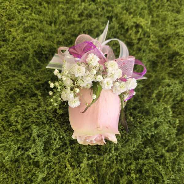Pink rose bud with white baby's breath and ribbon on green moss