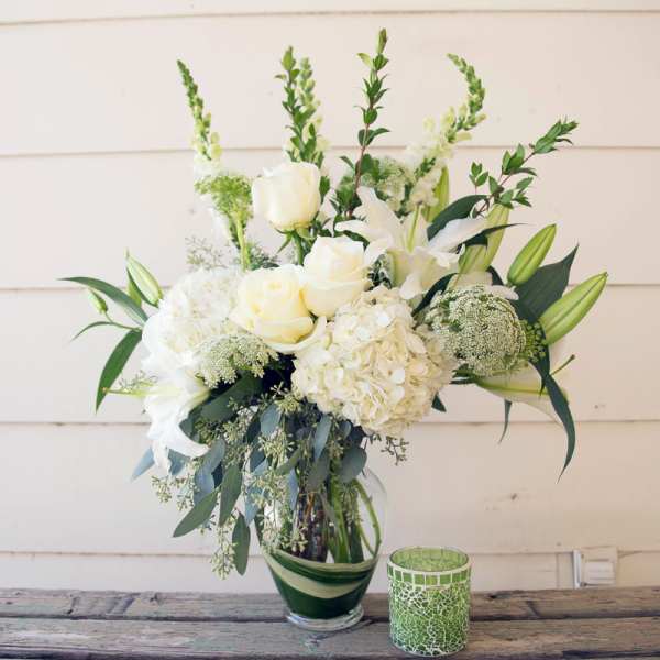 White floral arrangement in a glass vase with a green mosaic candle holder beside it