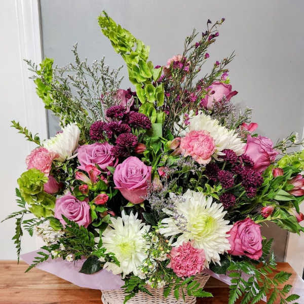 Basket arrangement of pink roses, white daisies, and purple flowers